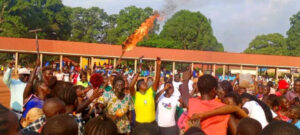 Crowd of football fans at Yambio Freedom Square, brandishing tools and fire.